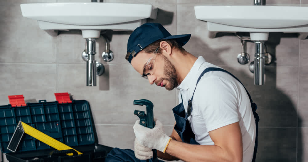 man with wrench under a sink