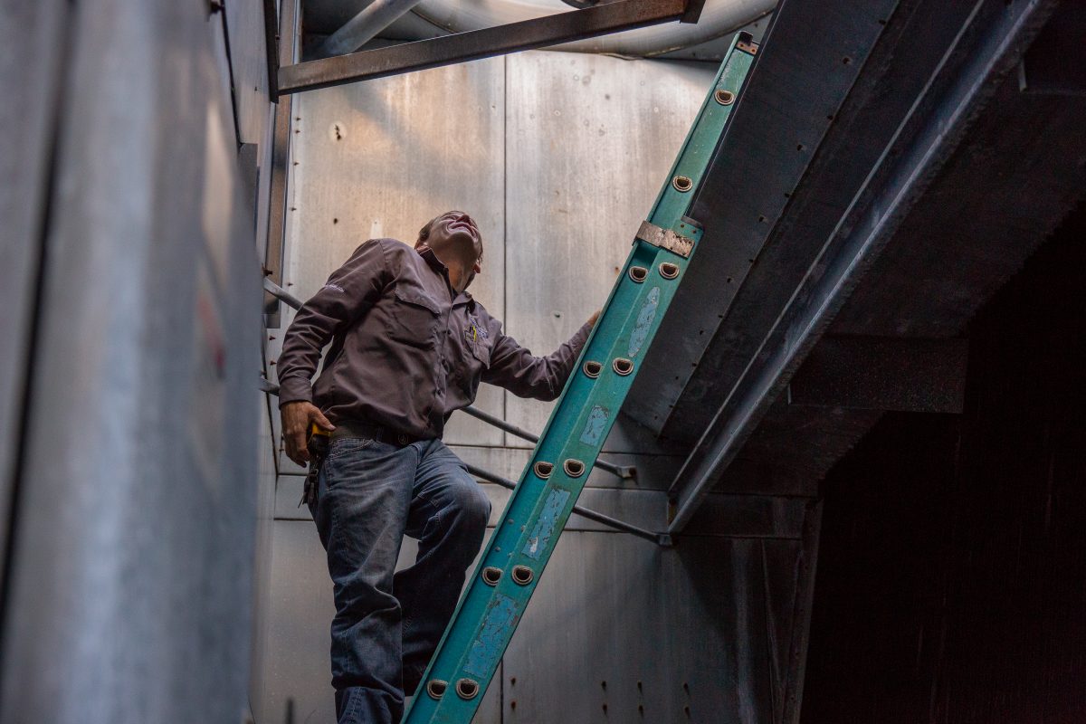 hvac pro standing on a ladder in an HVAC duct