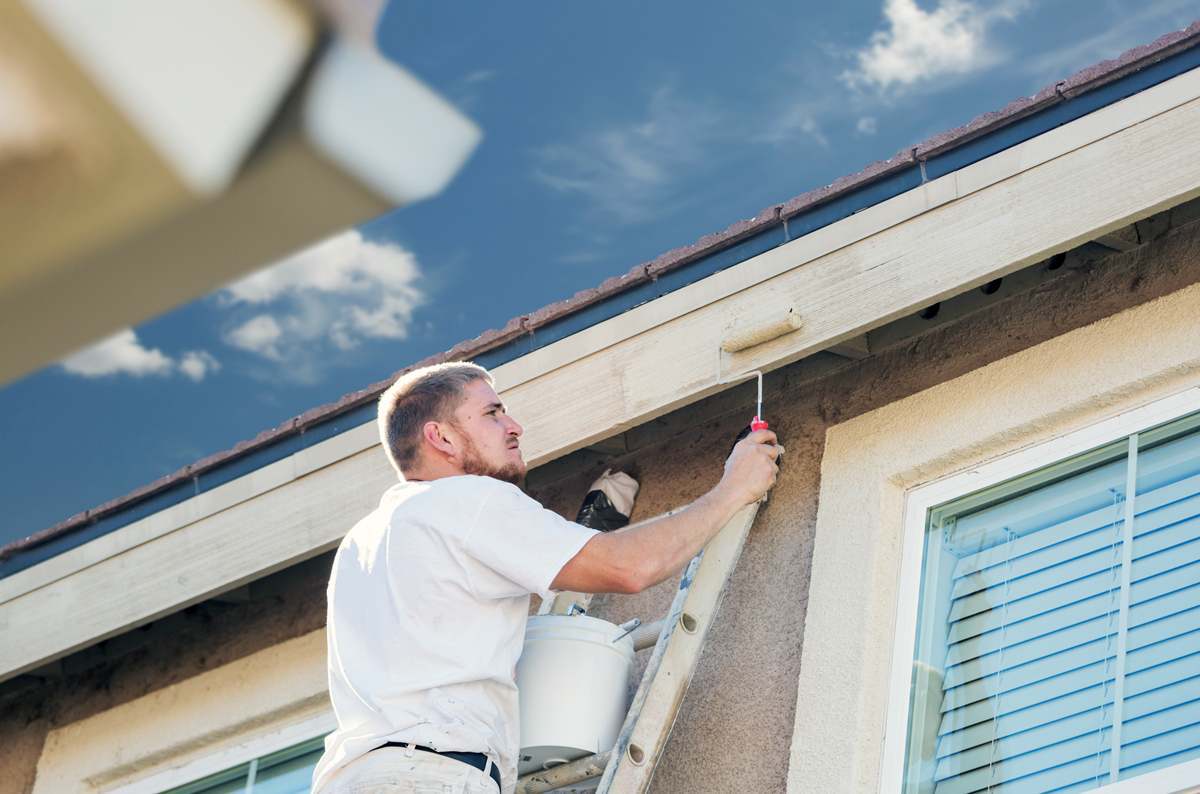 professional painter on a ladder painting the side of a house