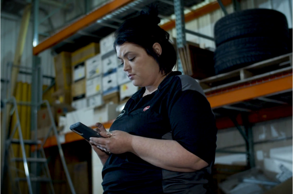 Woman using Housecall Pro app on phone in warehouse