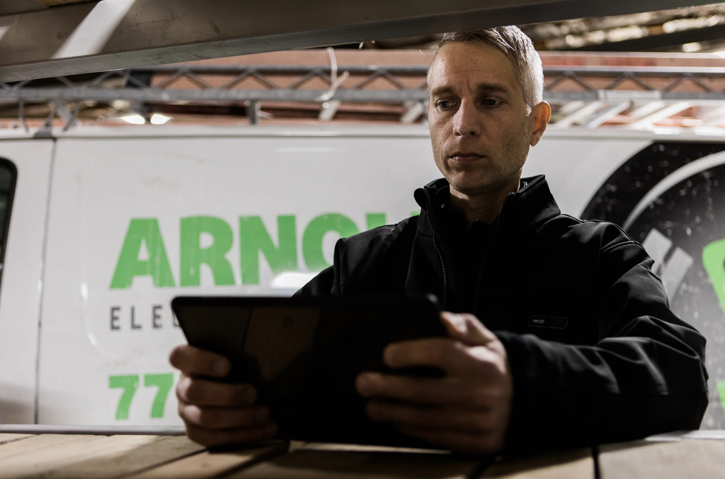 Arnold Electric electrician checking tablet with white work van in back