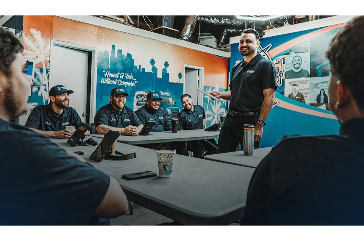 - Housecall Pro Team leader giving a presentation to service professionals during a meeting, with team members listening and smiling around a conference table.