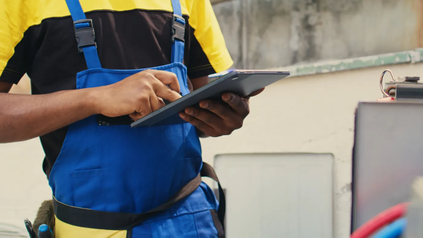 - Housecall Pro close up of skillful technician commissioned outside for hvac system routine maintenance looking at refrigerant issues using a tablet