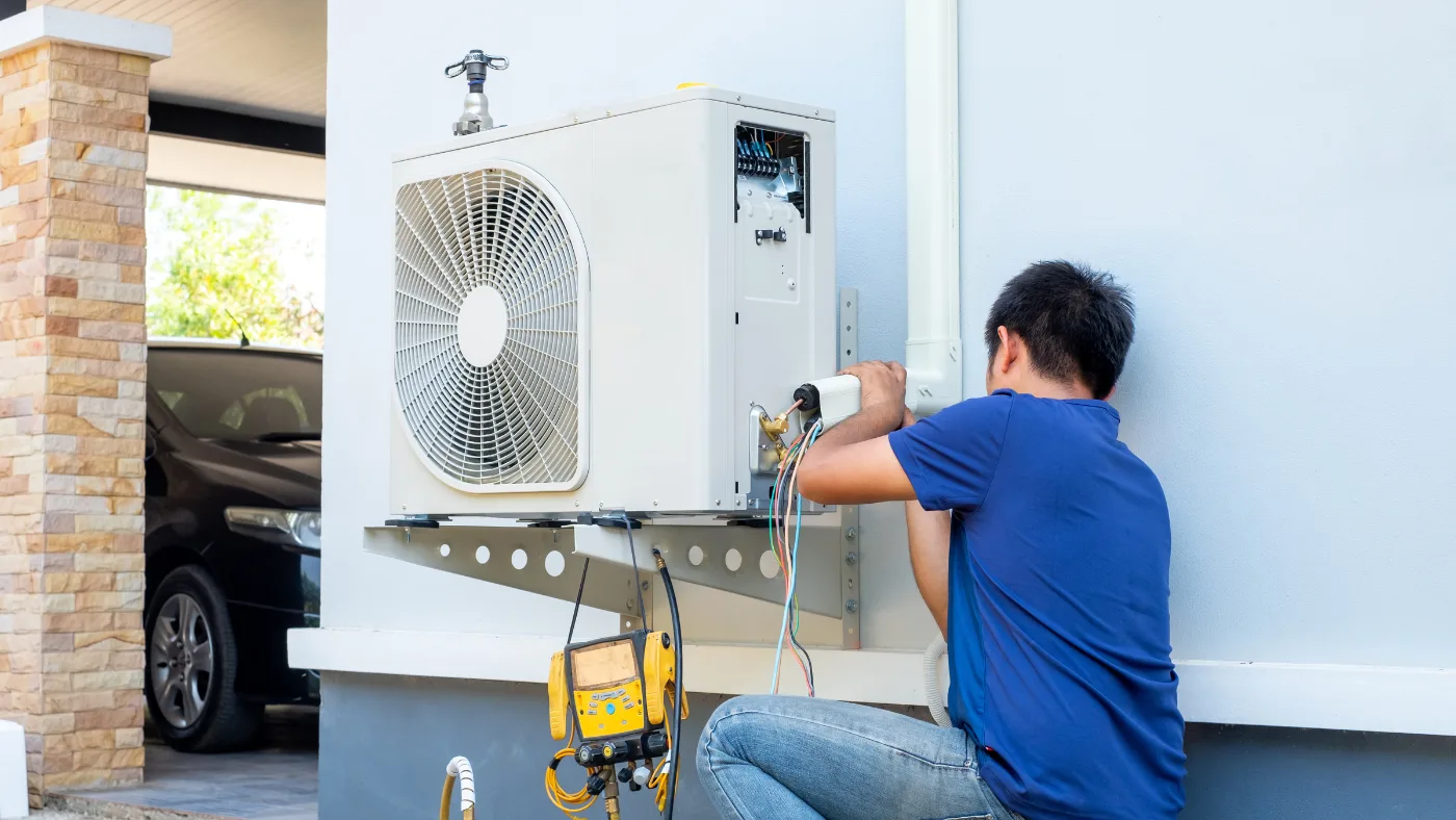 HVAC technician servicing an outdoor air conditioning unit at a residential property.