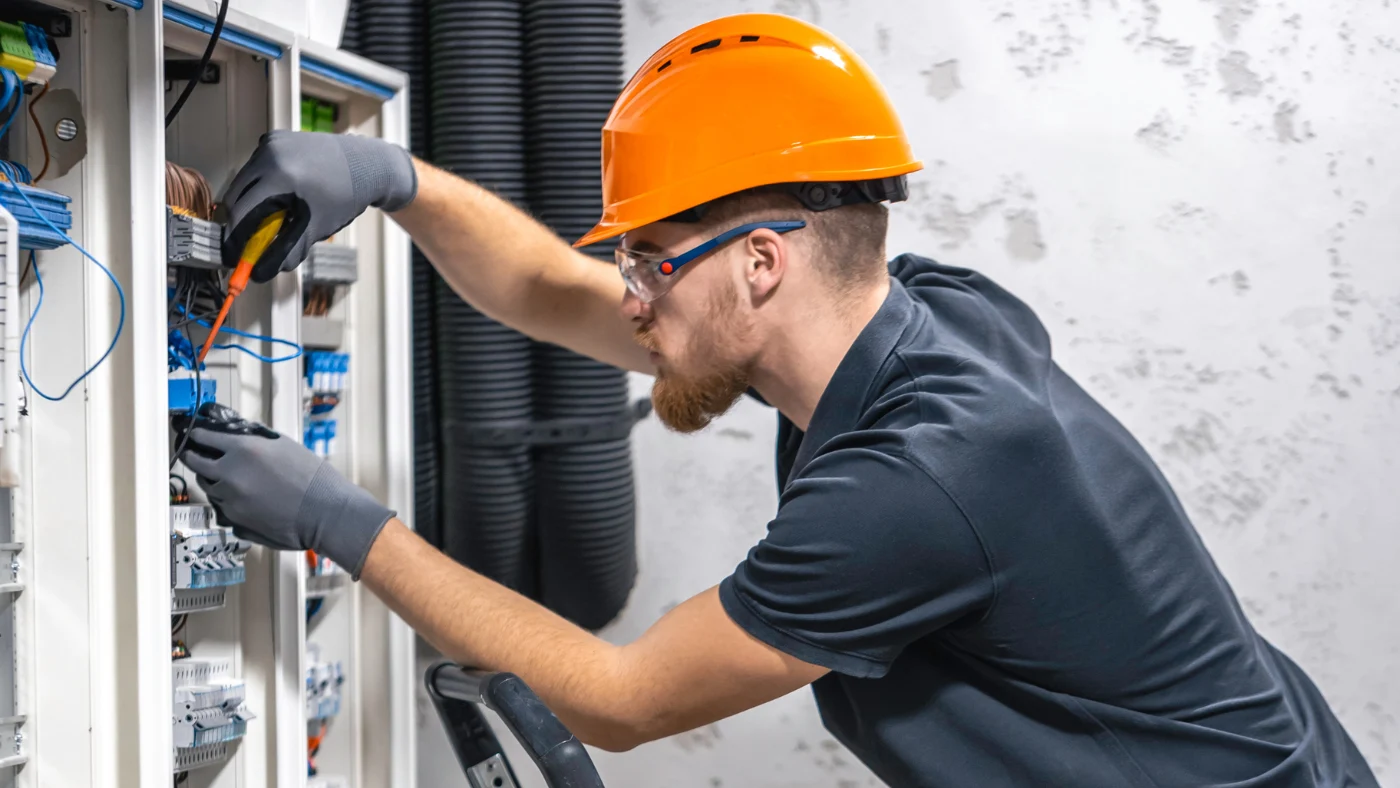 Professional electrician working on electrical wiring and circuit panels with safety gear.