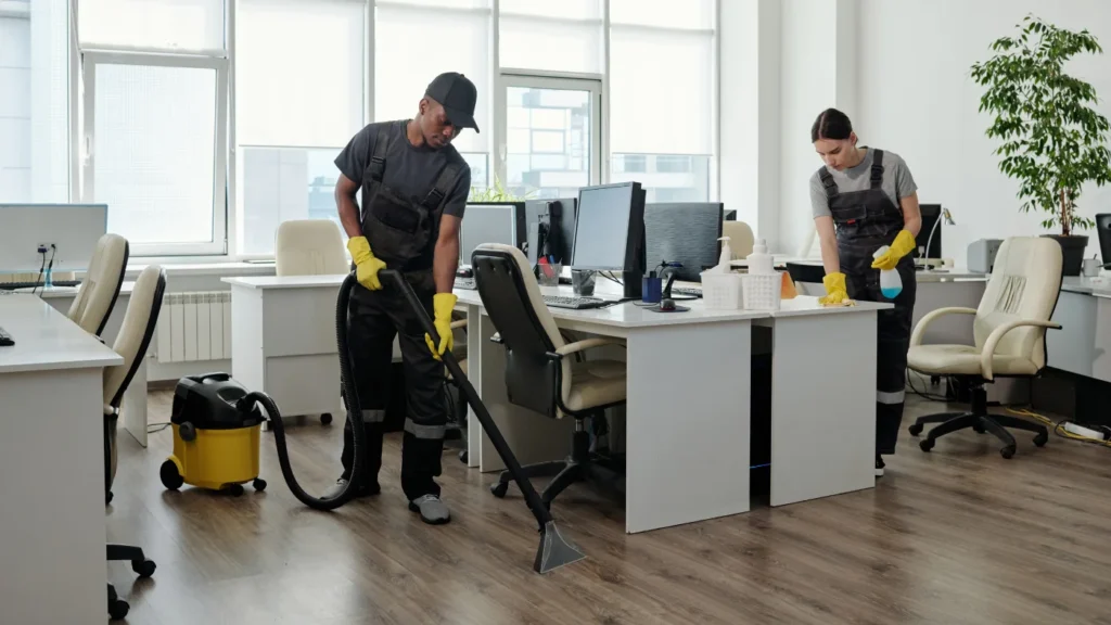 - Housecall Pro pro using vacuum cleaner for cleaning floor while a woman cleaning the desk