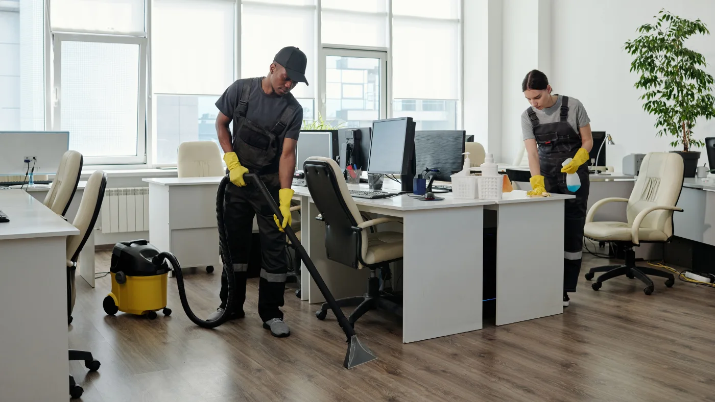 pro using vacuum cleaner for cleaning floor while a woman cleaning the desk