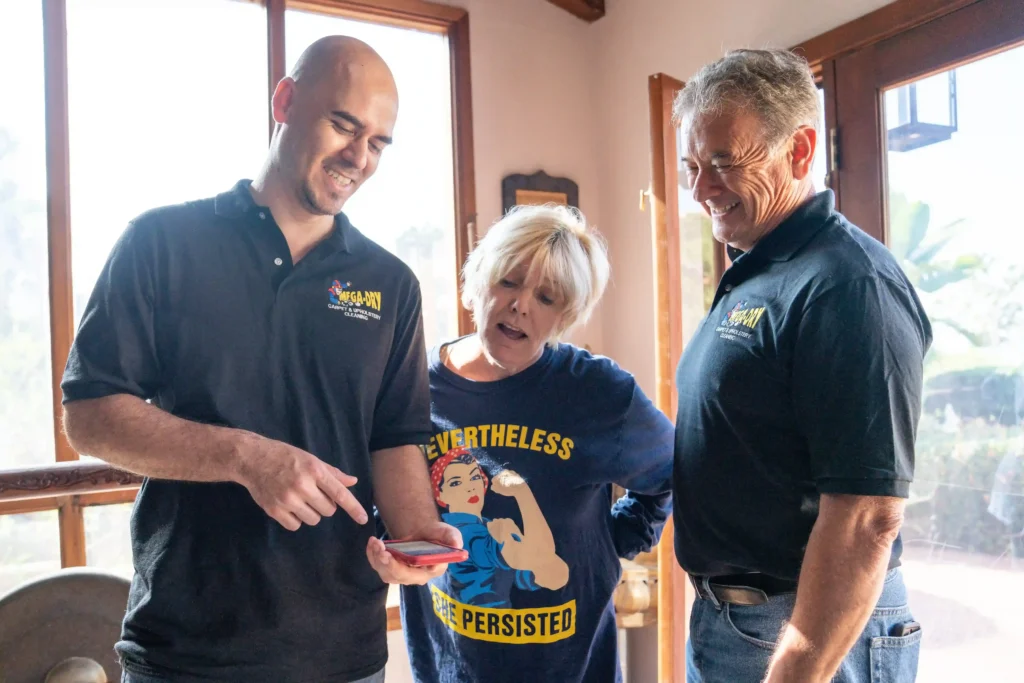 - Housecall Pro Two service professionals showing a customer information on a smartphone while standing together inside a home.