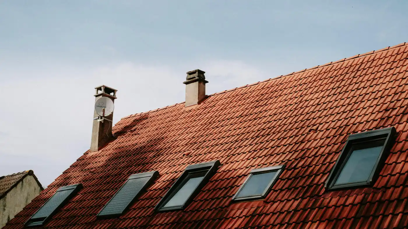 Red tiled roof with skylights and chimney under clear sky