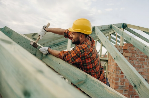 Pro Construction worker is on the roof of a house with hammer in hand