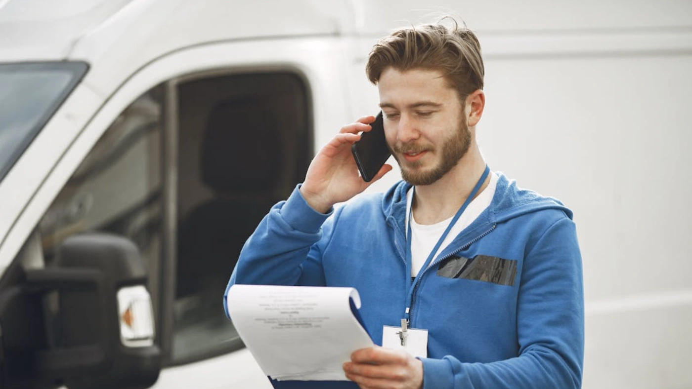 Contractor reviewing paperwork while talking on phone beside service van