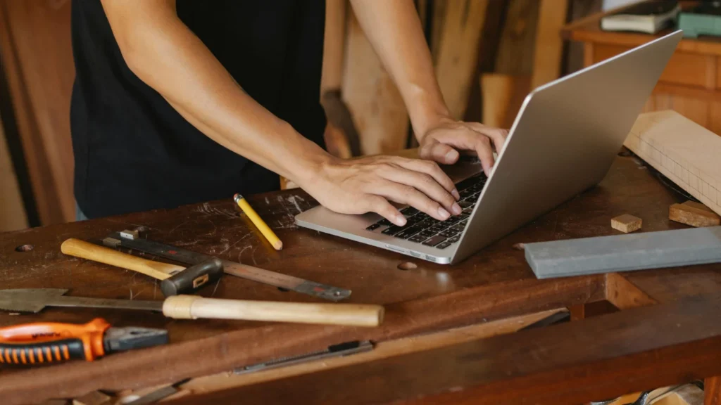 man standing in his workshop and using laptop on a table