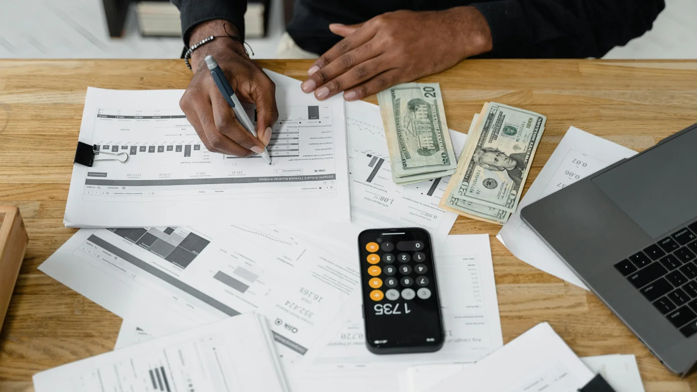 Business owner reviewing financial reports and planning taxes with calculator and cash on desk