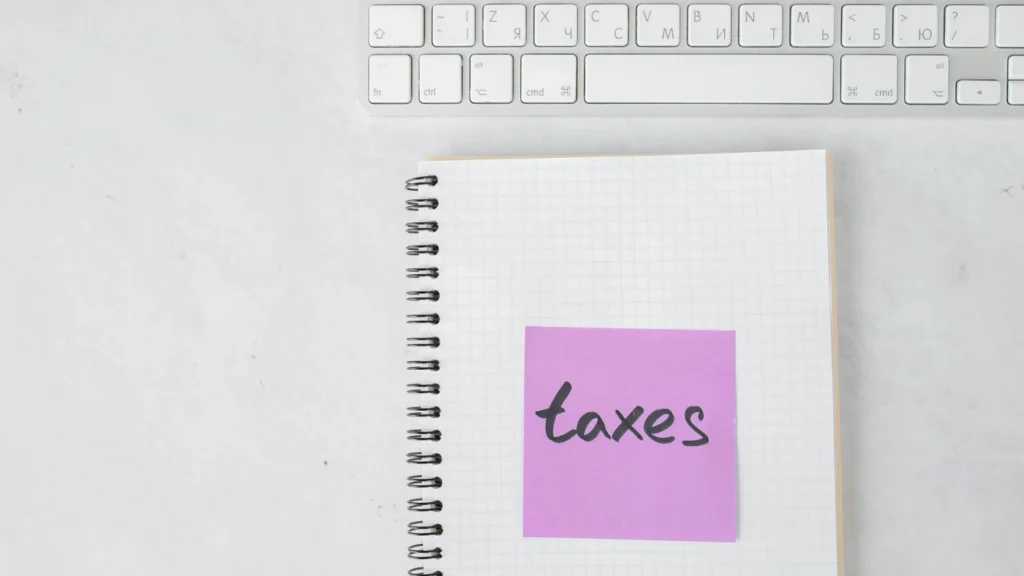 Sticky note labeled “taxes” on notebook beside keyboard