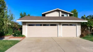 Suburban house with a three-car garage and driveway under a clear blue sky.