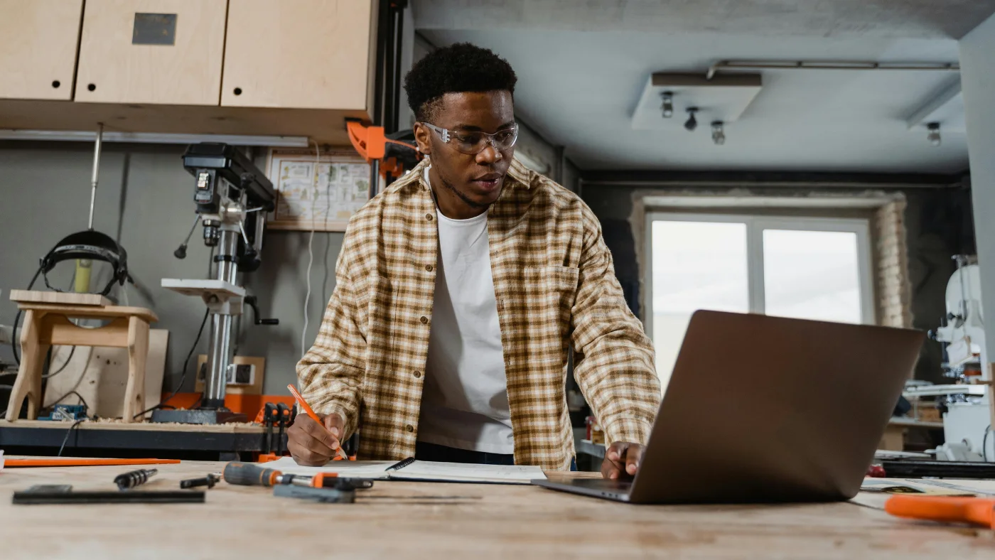 Pro carpenter looking at laptop and writing on a notebook