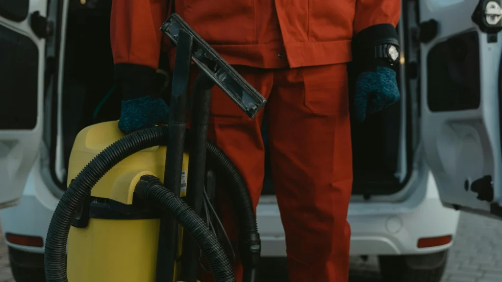 Cleaner in red uniform holding a vacuum in front of a van.