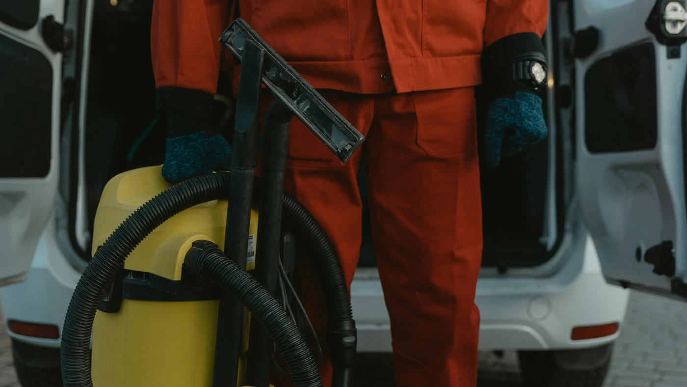 Cleaner in red uniform holding a vacuum in front of a van.