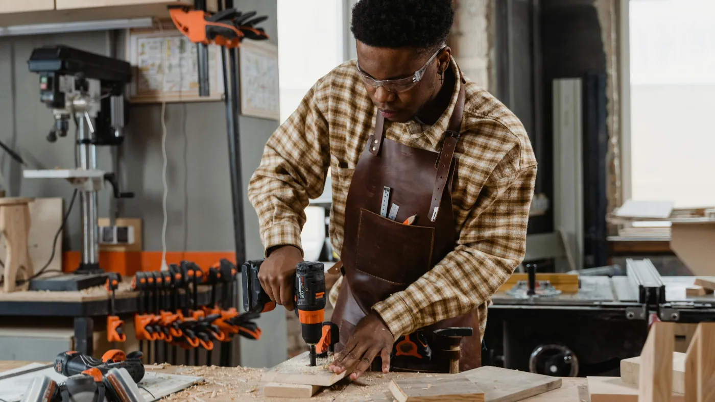 Man in a workshop drilling wood on a wooden table