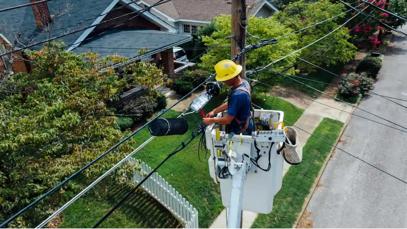 Utility worker in a bucket repairing overhead cables in a residential area.