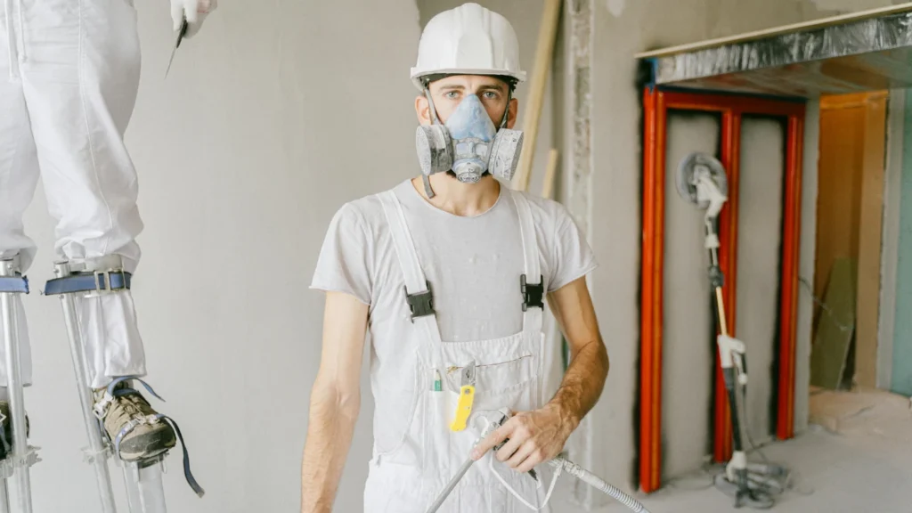 Professional painters working inside a house, one wearing a mask and using a spray gun
