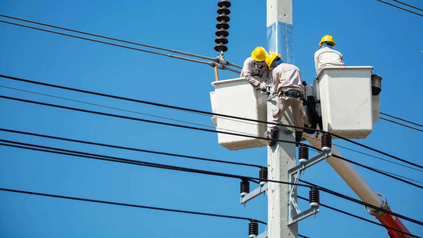 Electrical lineworkers repairing power lines from bucket truck, representing different types of electricians