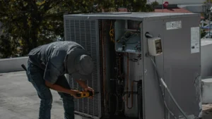 Technician repairing a rooftop HVAC unit with a power drill.