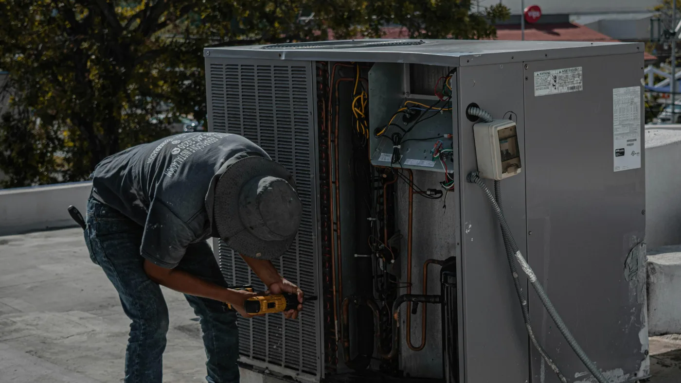 Technician repairing a rooftop HVAC unit with a power drill.