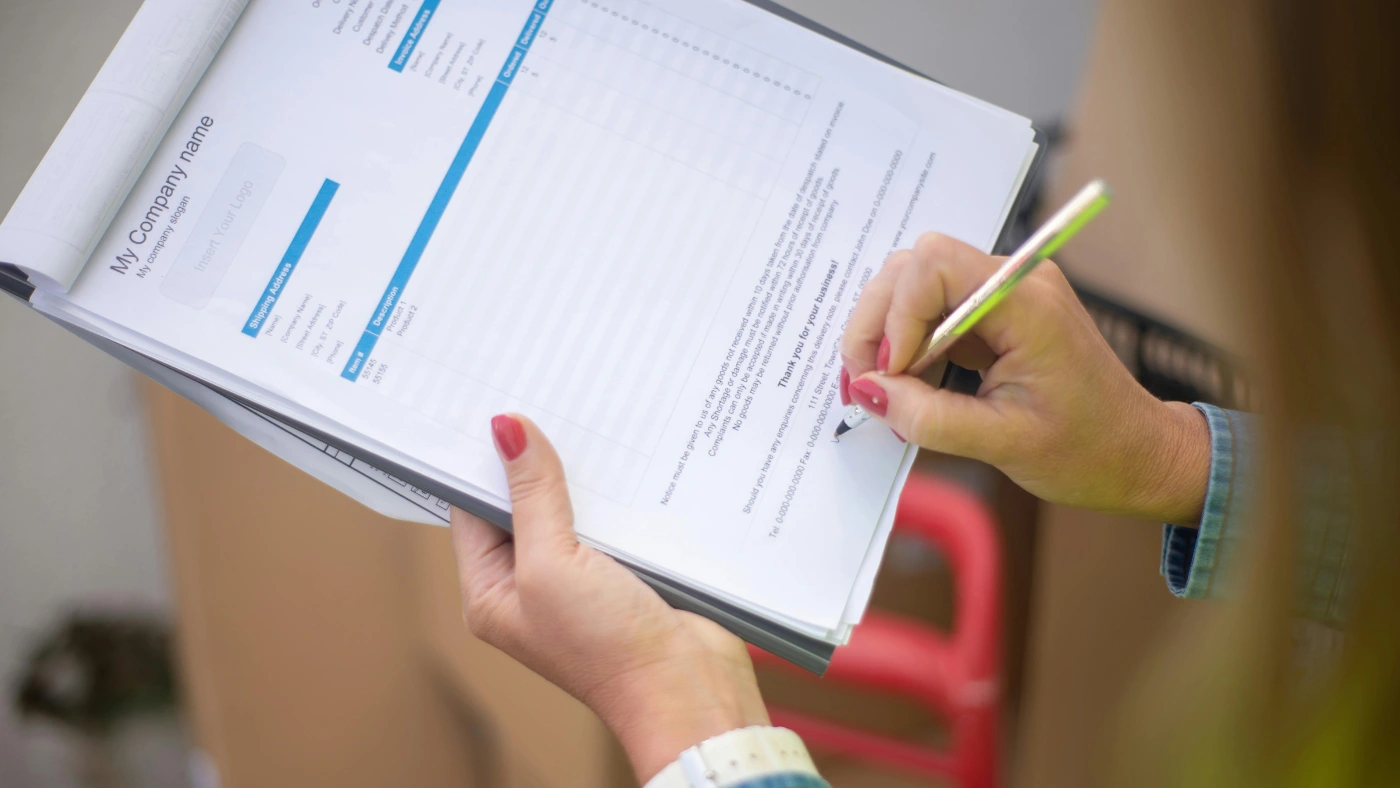 A woman holding an invoice and a pen, signing the document