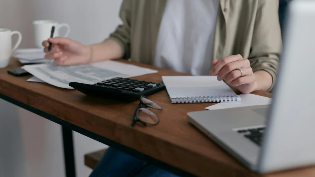 Person calculating expenses at desk with laptop and calculator