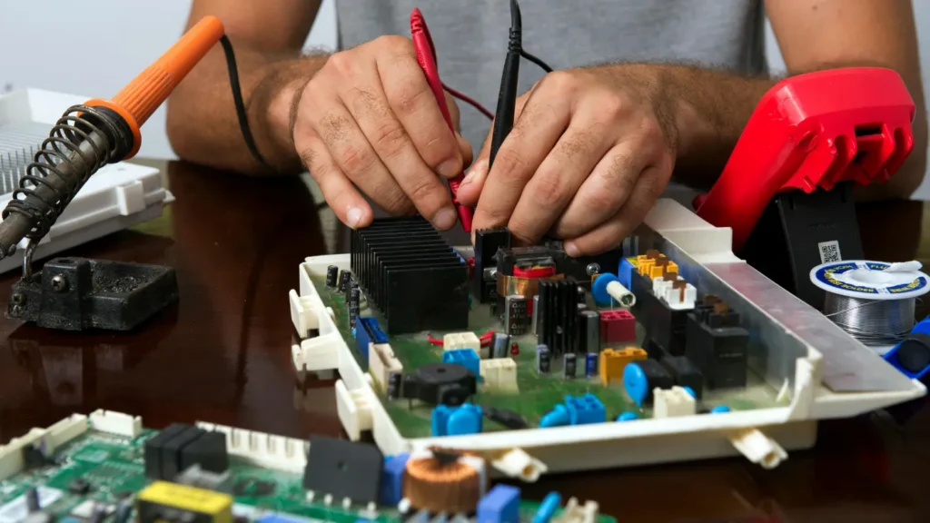 Technician testing an appliance control board with a multimeter and soldering tools