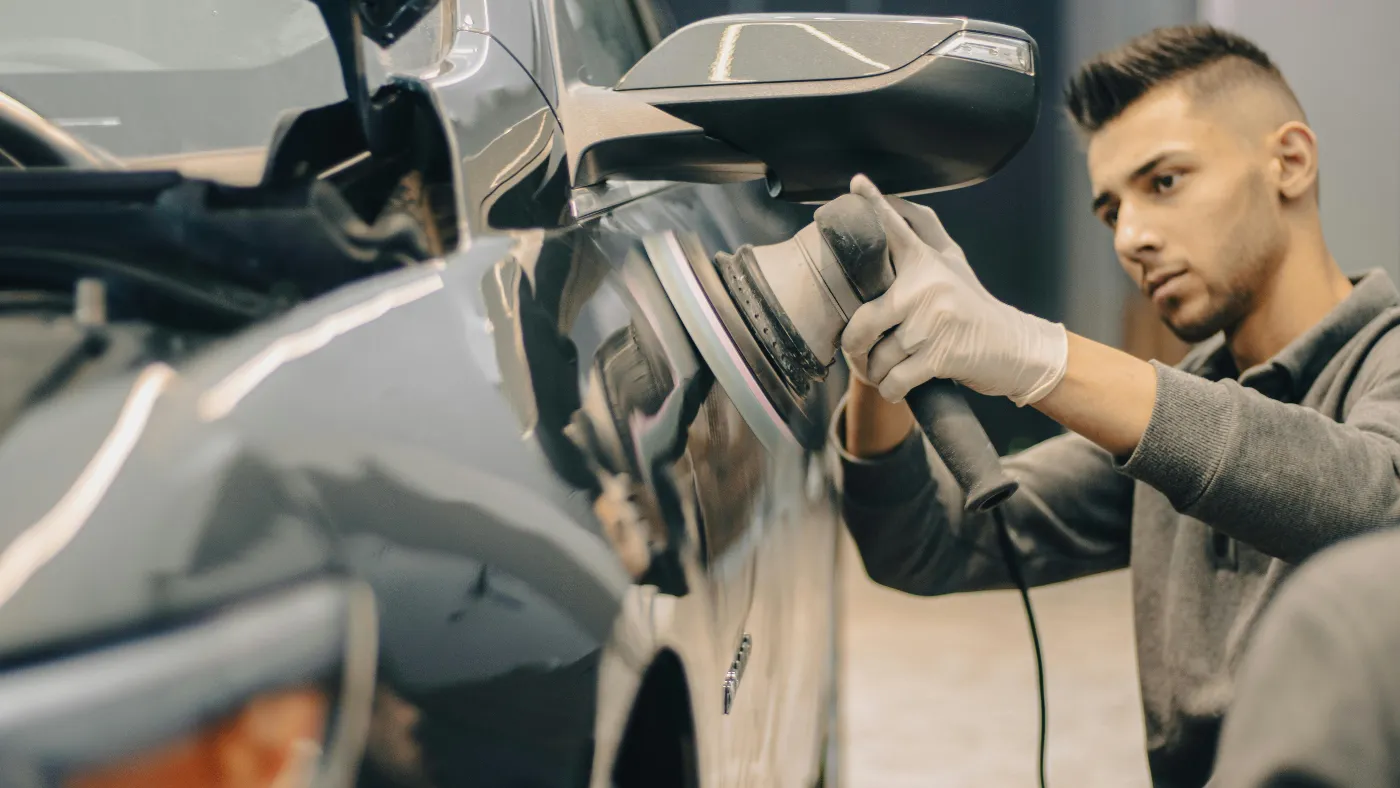 Auto detailing technician polishing the side of a car with a buffer