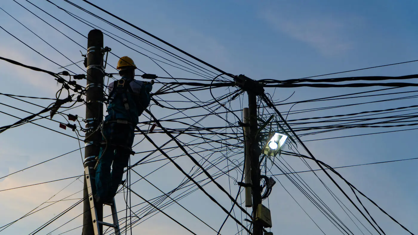 Worker on a ladder repairing dense overhead power lines on utility poles.