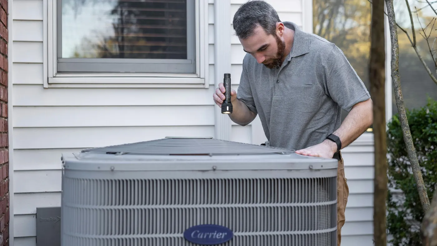 HVAC technician inspecting an outdoor air conditioning unit at a home