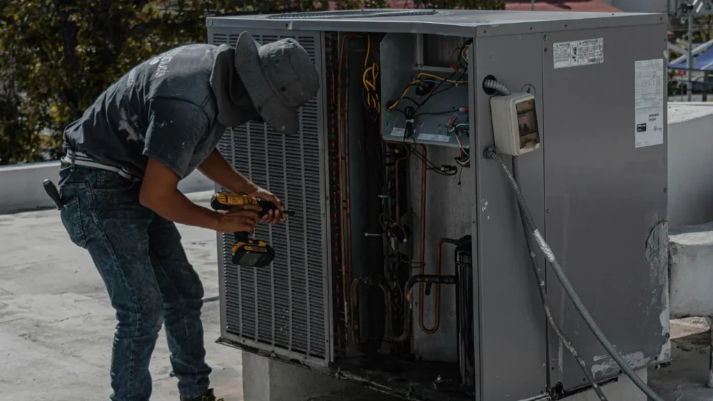 HVAC technician repairing a rooftop air conditioning unit with a drill