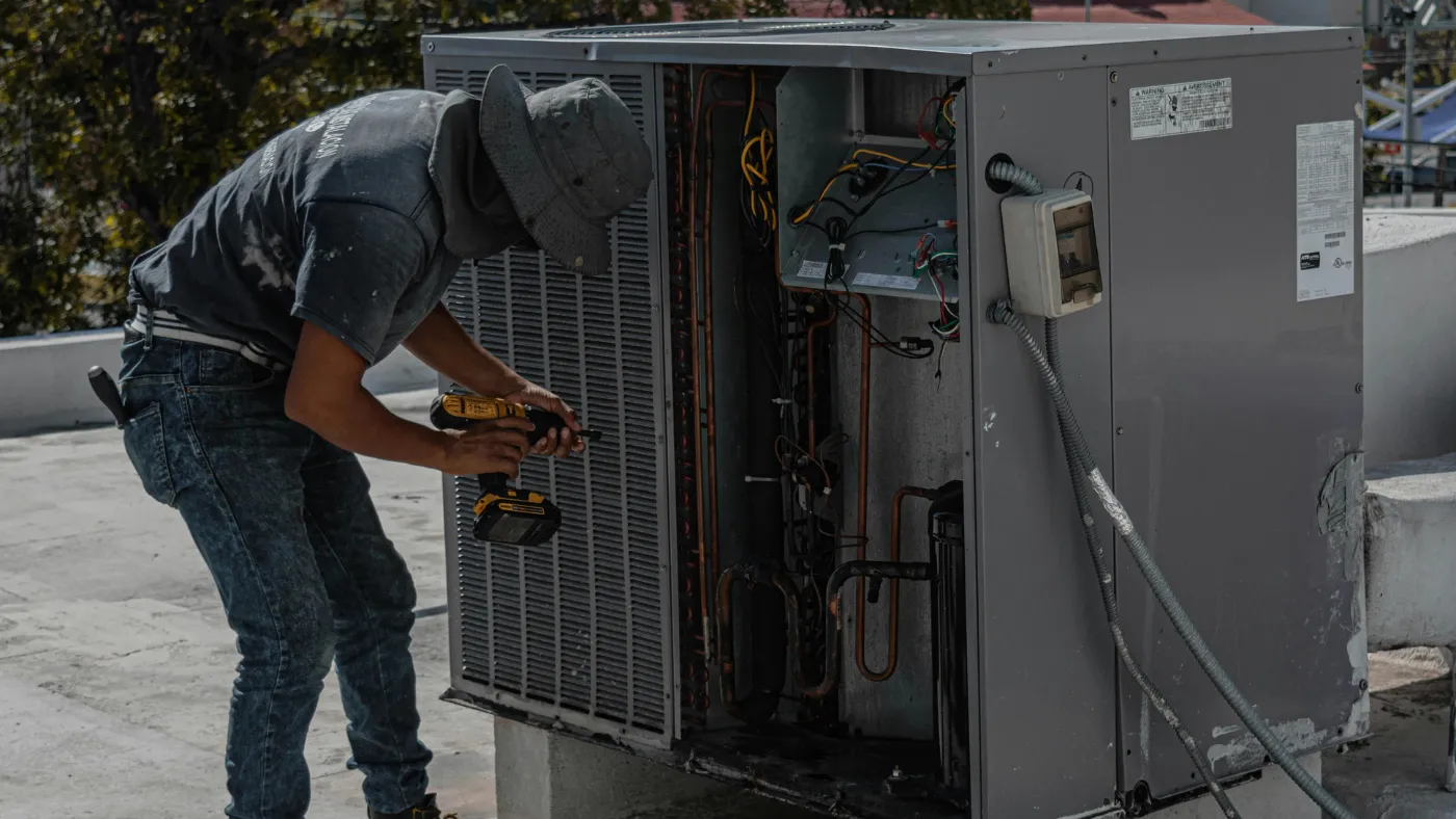 HVAC technician repairing a rooftop air conditioning unit with a drill
