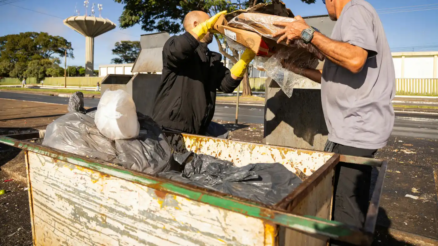 Junk removal workers loading trash and cardboard into a dumpster