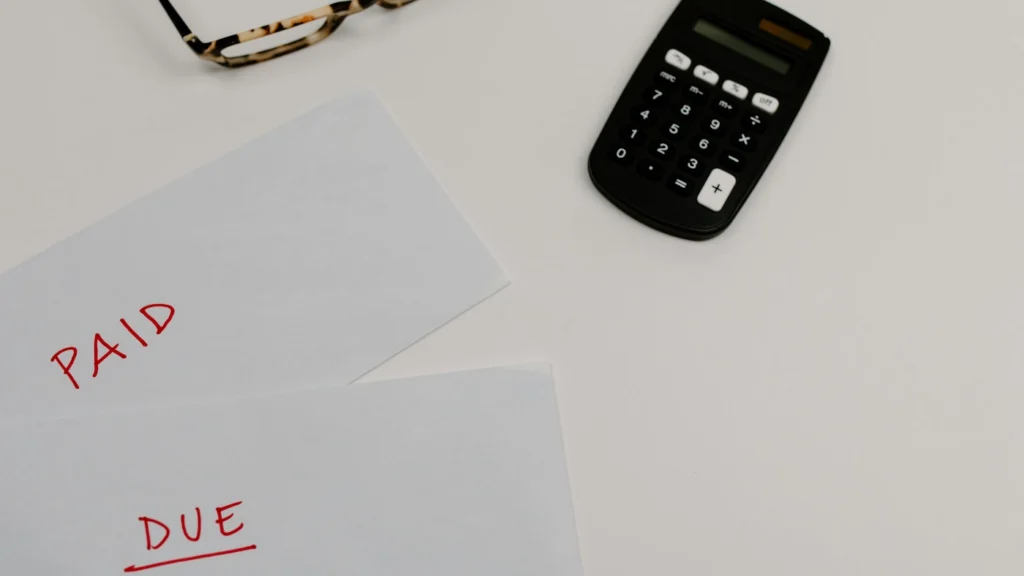 Bills marked “paid” and “due” beside calculator on desk