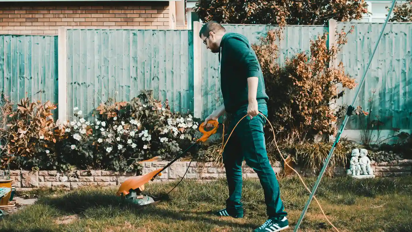 Landscaper trimming grass with an electric string trimmer in a backyard