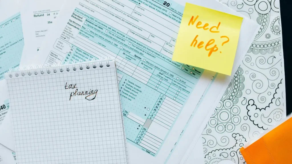 Tax forms and notebook labeled “tax planning” with sticky note reading “Need help?”