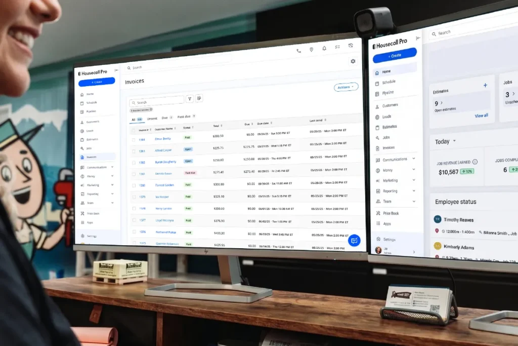 A smiling home service business owner sits at a desk with two monitors displaying the Housecall Pro web app. The left screen shows the Invoices list with customer names, statuses, and due dates. The right monitor displays the updated Housecall Pro navigation with the Home dashboard showing job revenue of ,587 and employee status for two technicians.