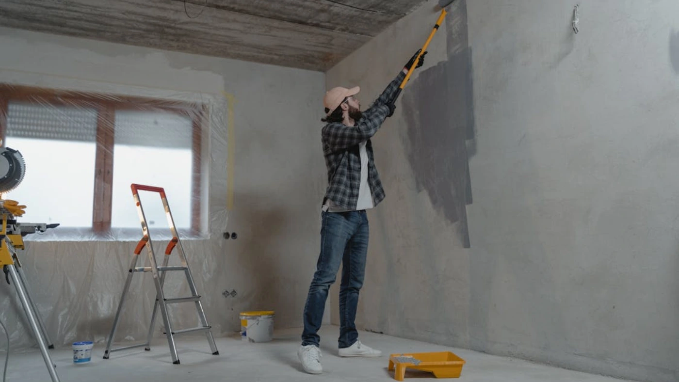 Professional house painter applying fresh gray paint to an interior wall during home renovation project