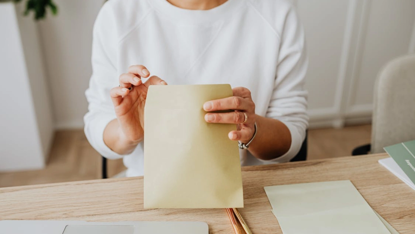 Person holding a mailer envelope at desk for direct mail marketing campaign