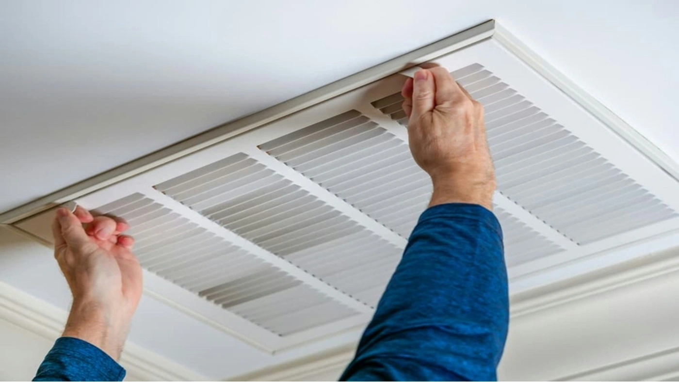 Homeowner replacing HVAC return air filter in ceiling vent for improved system performance