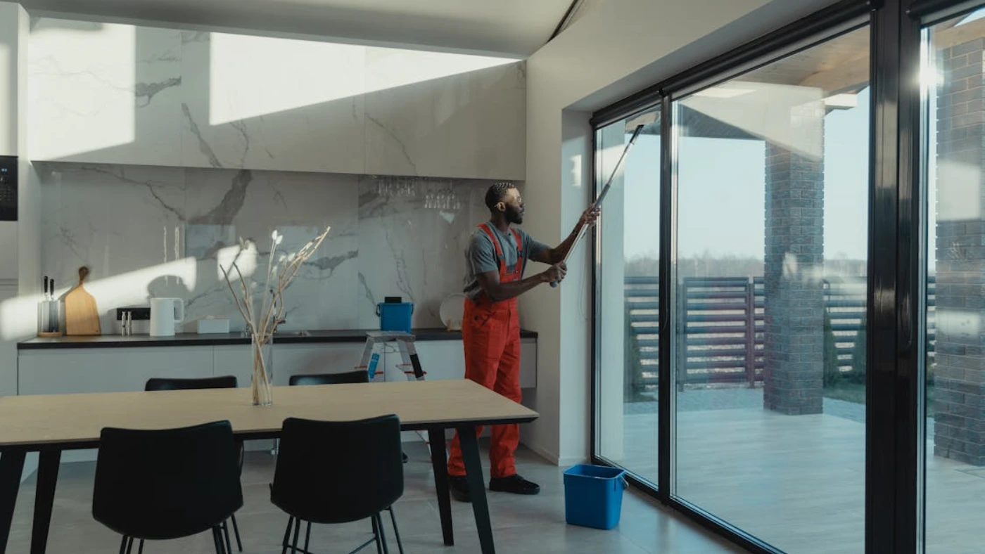 Professional cleaner washing large glass doors in modern home interior