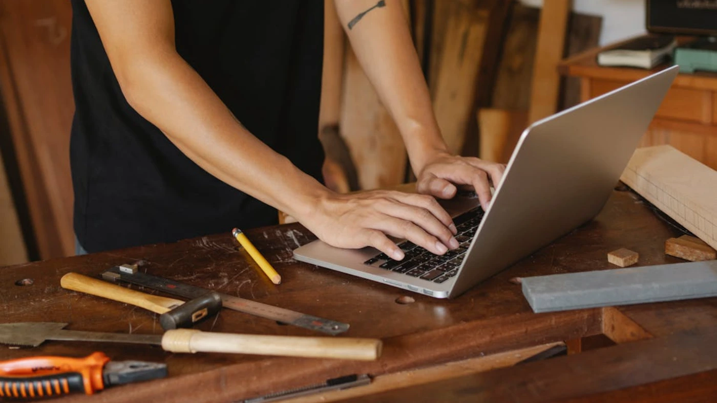 Handyman using laptop at workbench to build a website.