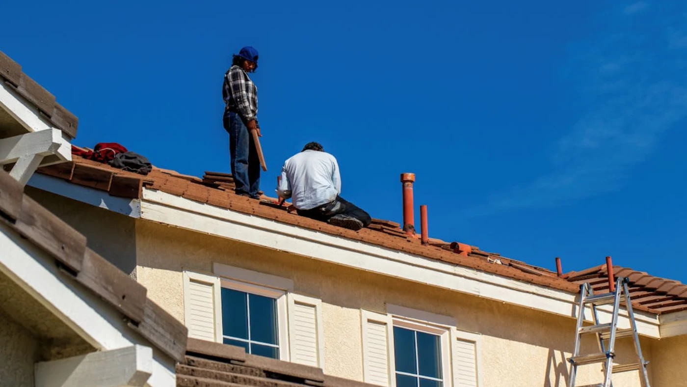 Roofers installing shingles on residential home roof under clear blue sky