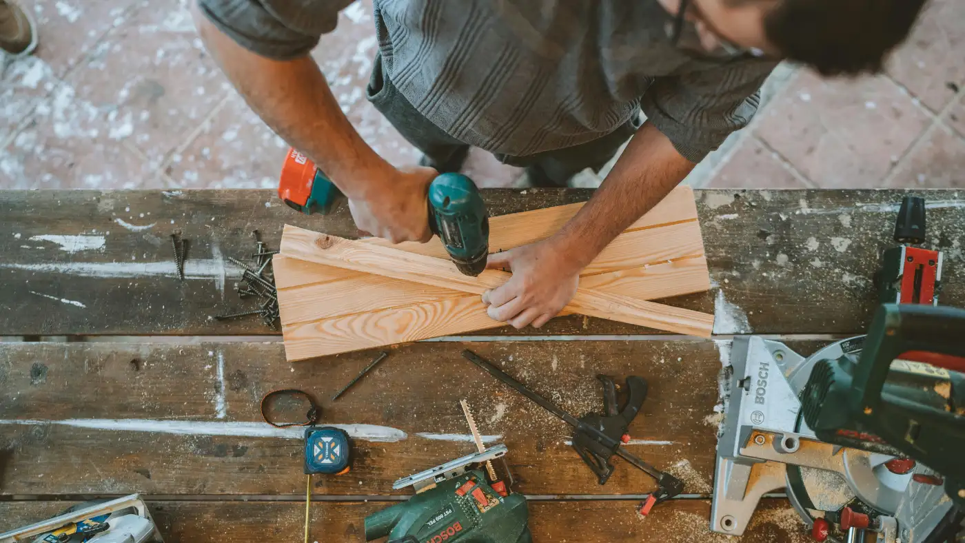 man drilling wooden planks in a workshop