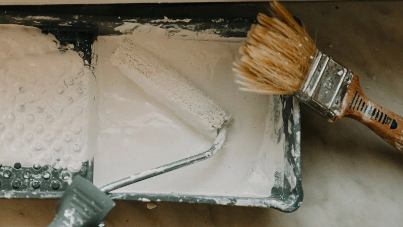 Paint roller and brush in tray with white paint, representing marketing strategies for a painting business