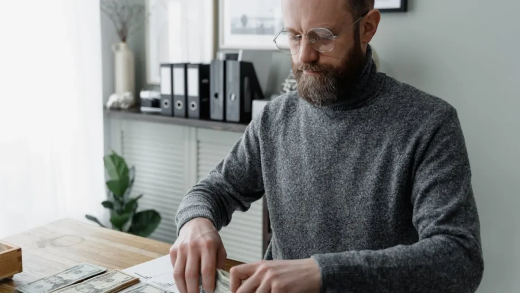 Business owner organizing cash and reviewing documents at desk while setting up payroll for a small business